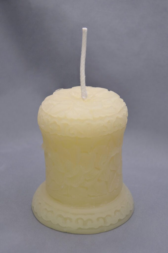 Yellow candle with white wick and ornate base.